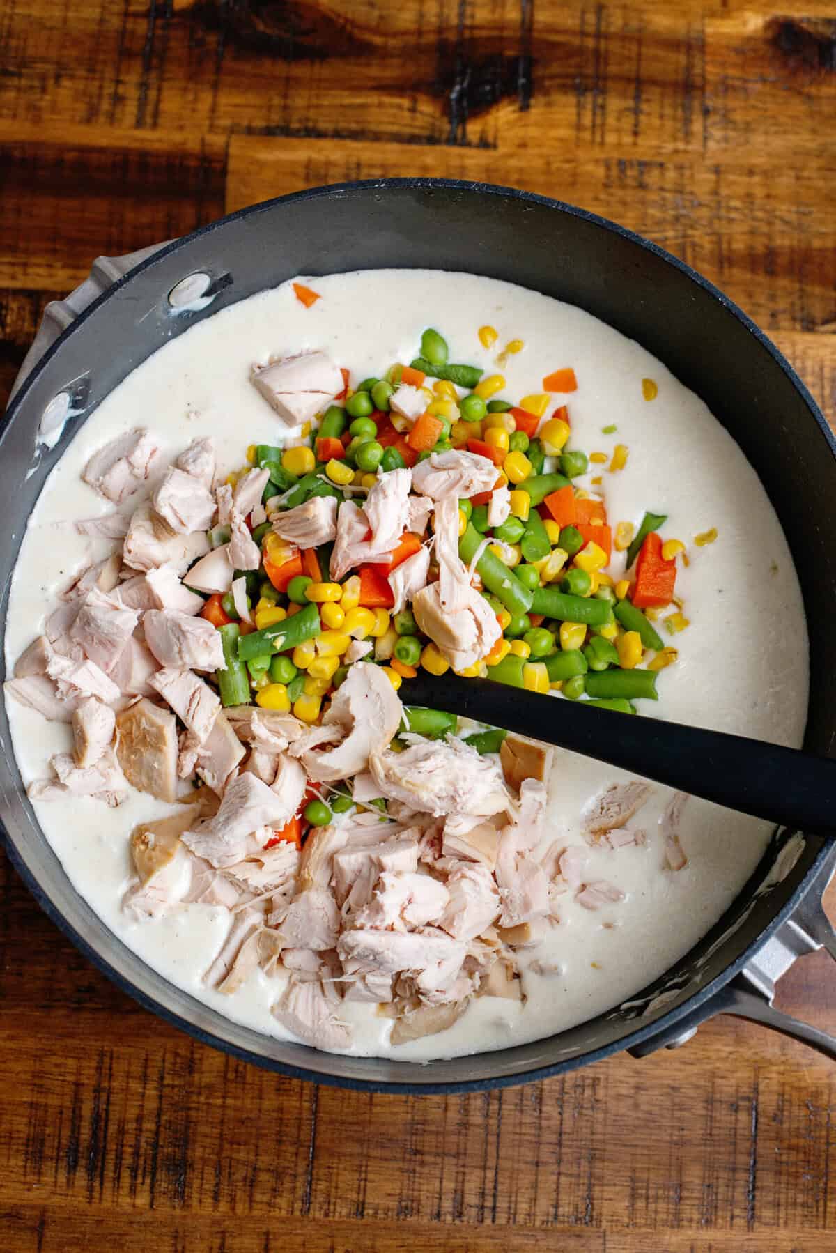A saucepan with diced, cooked chicken with mixed vegetables in a creamy sauce.