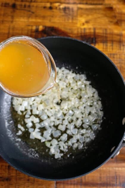 Pouring chicken broth in a saucepan of melted butter and onions.
