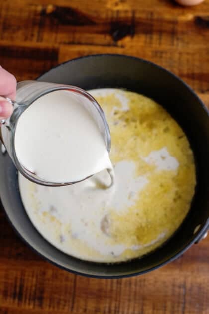 Adding cream to a saucepan of butter, onions, chicken broth, and flour.