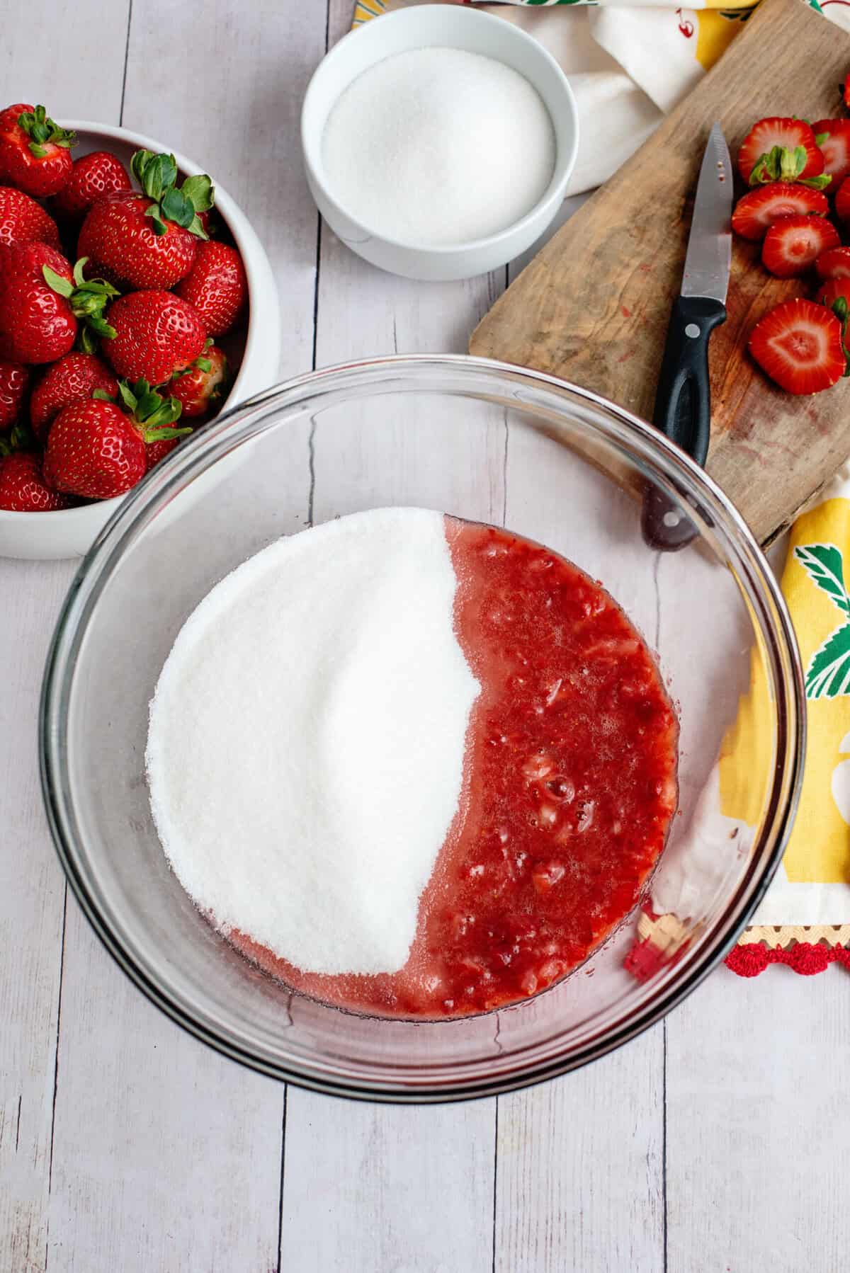 Adding sugar to the bowl of crushed strawberries