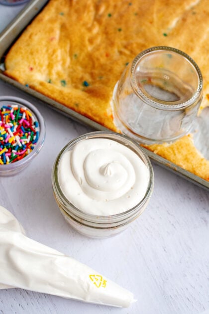 Adding the final layer of vanilla frosting to a Funfetti dot cake jar