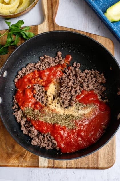 Stirring marinara sauce, Italian seasoning, garlic powder, onion powder, salt, and black pepper into the pan with ground beef