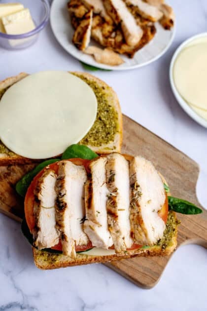 Adding sliced chicken breast to pesto chicken panini sandwich