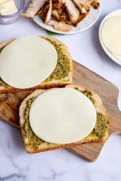 Adding provolone cheese to the slices of bread with pesto