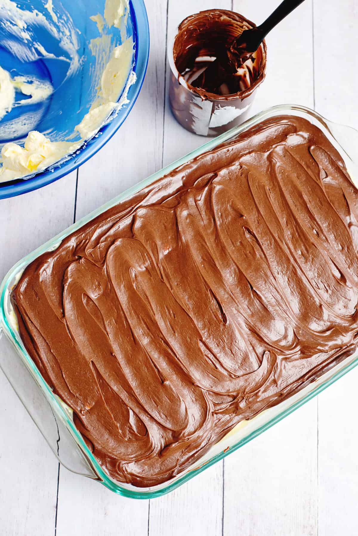 Spreading a layer of chocolate topping on the graham cracker and vanilla pudding layers