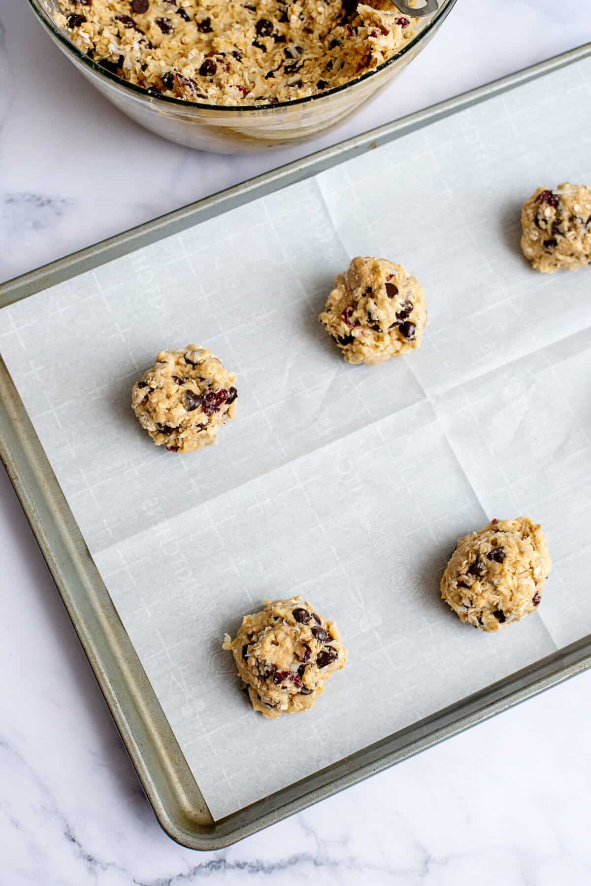 Adding chocolate chip oatmeal cookie dough balls to a baking sheet