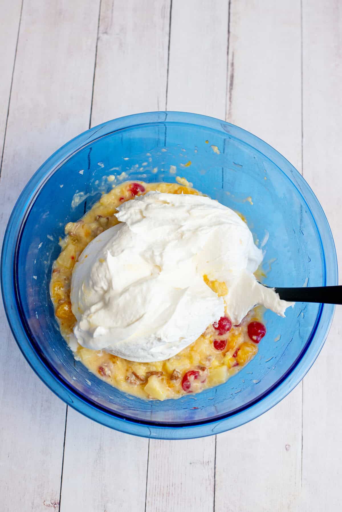 Adding the whipped topping to the bowl of Whoa Horsey salad fruits and nuts
