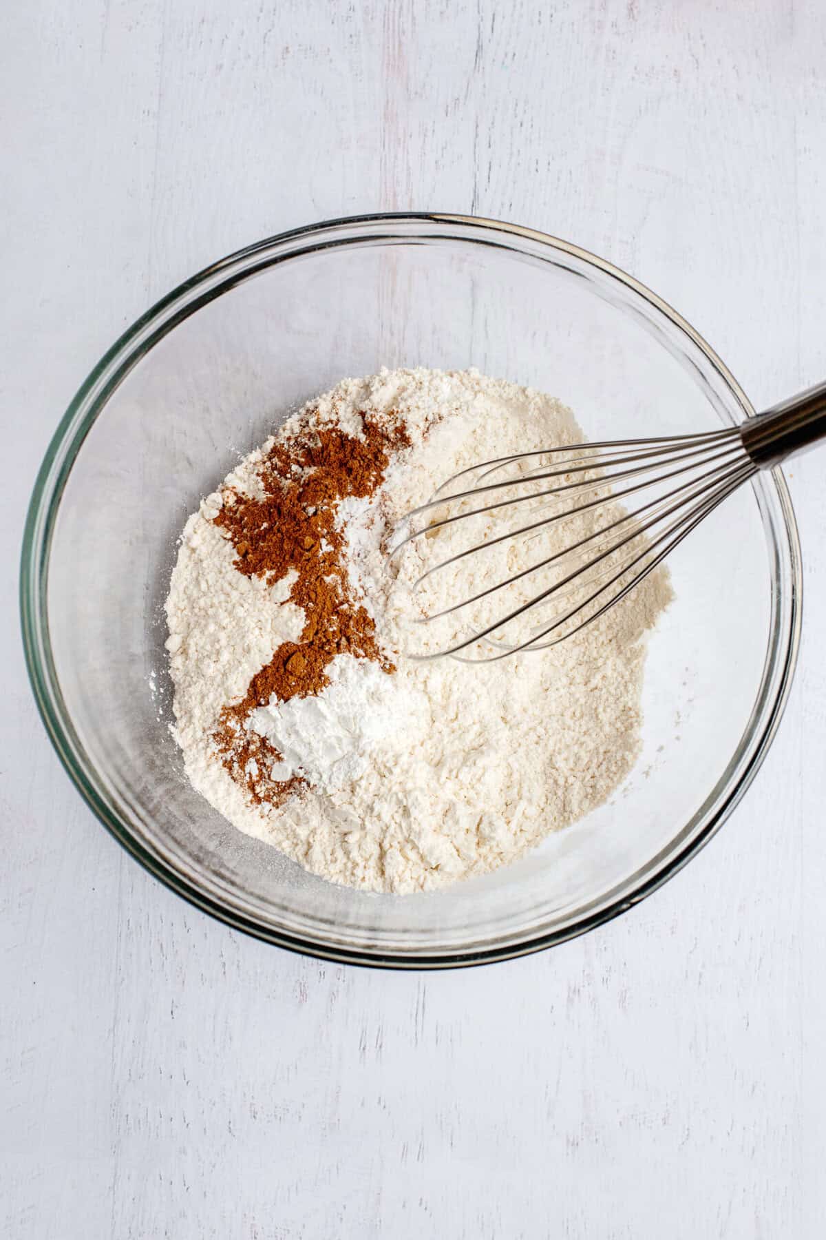 Flour, baking powder, baking soda, salt, and apple pie spice in a glass mixing bowl.