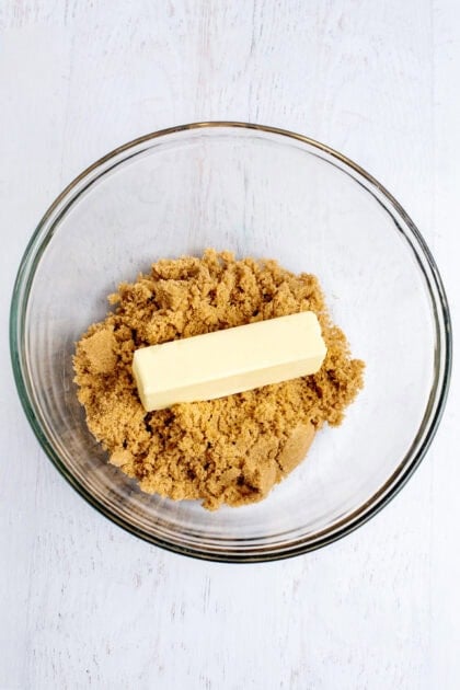 A stick of butter and brown sugar in a glass mixing bowl.