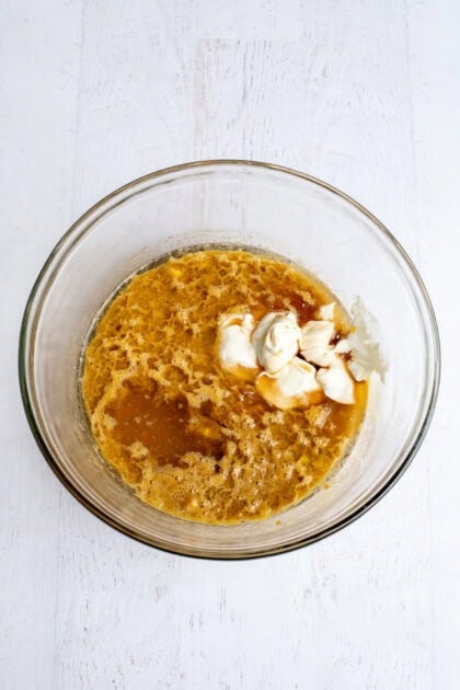 Eggs, apple cider, and sour cream in a glass mixing bowl.