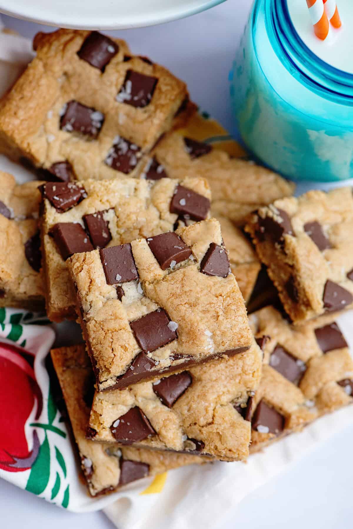 Chocolate chip cookie bars stacked on each other beside a glass of milk.