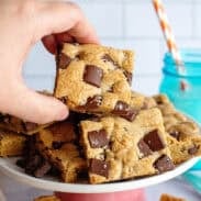 A hand holding a chocolate chip cookie bar with more in the background.