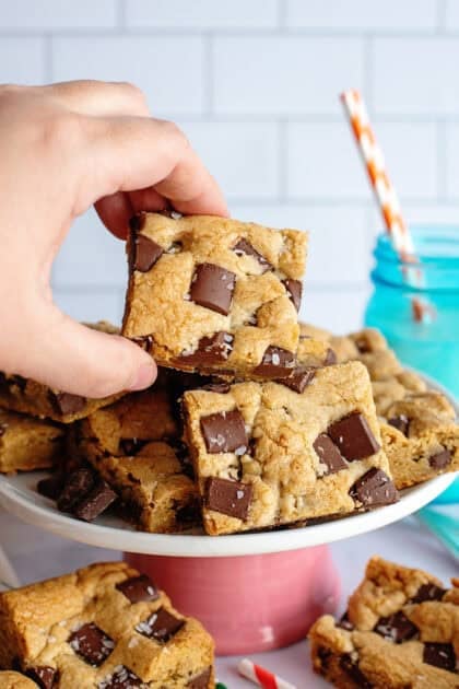 A hand holding a chocolate chip cookie bar with more in the background.