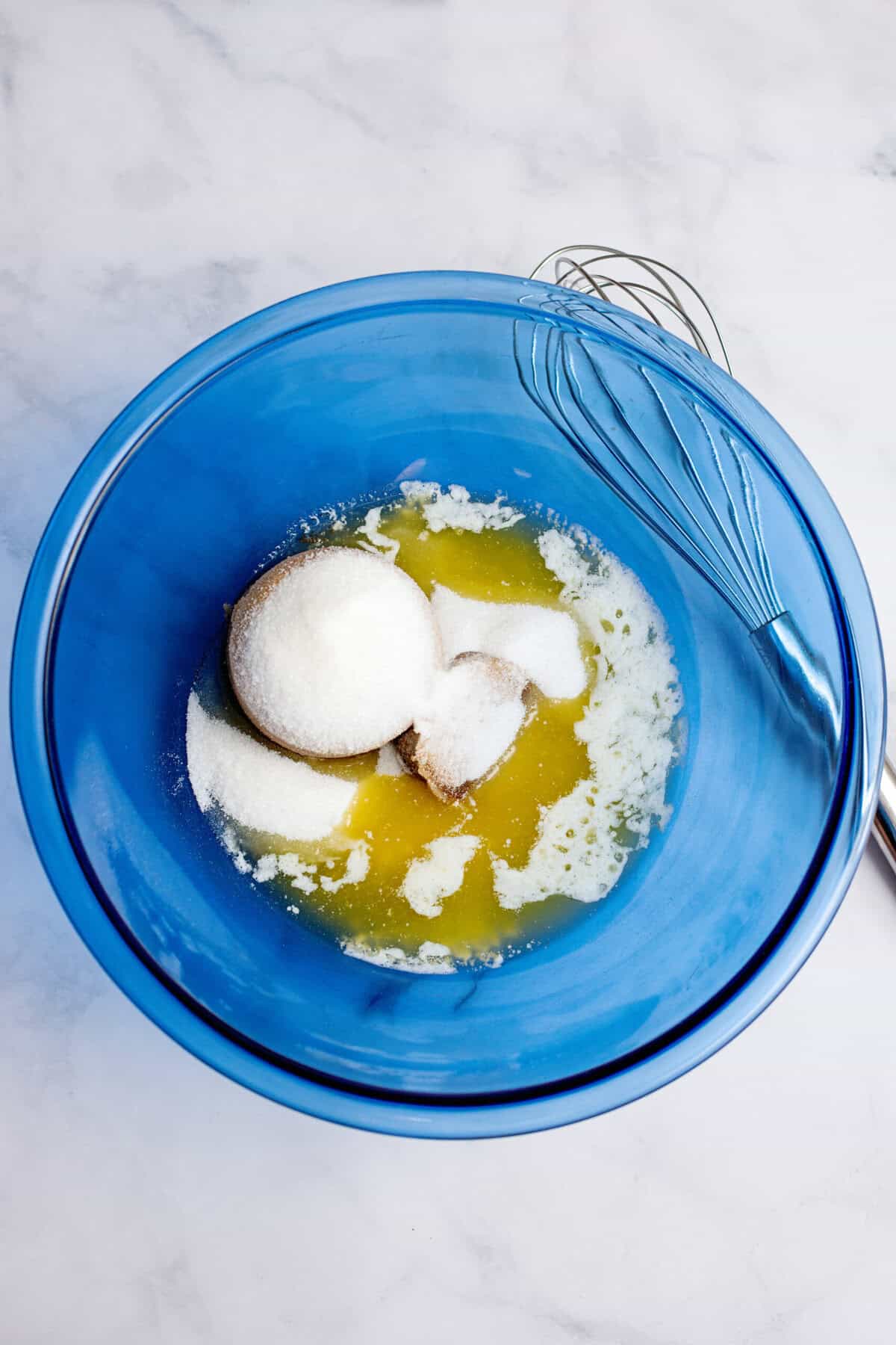 A glass blue mixing bowl with melted butter and brown and granulated sugar.