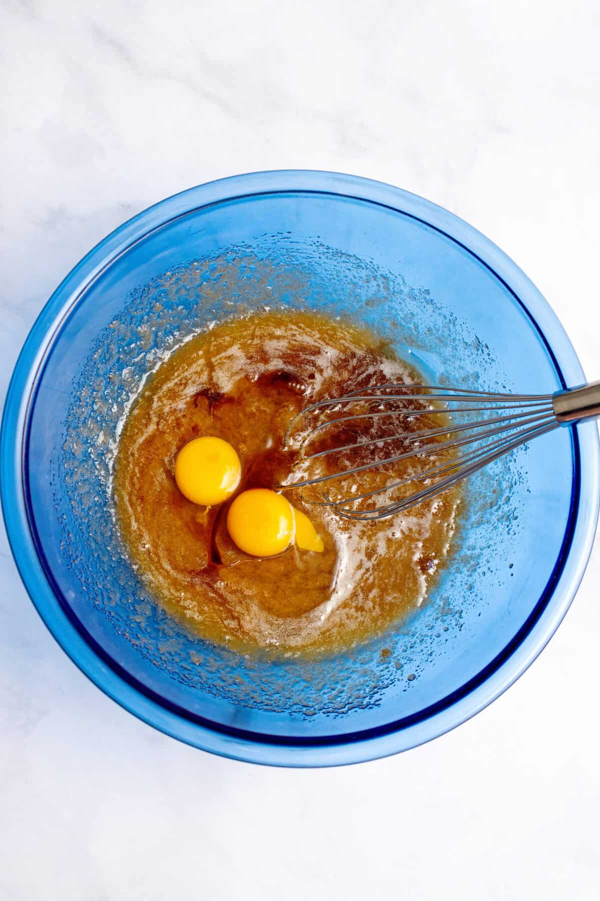 Whisking eggs and vanilla into a glass blue mixing bowl.