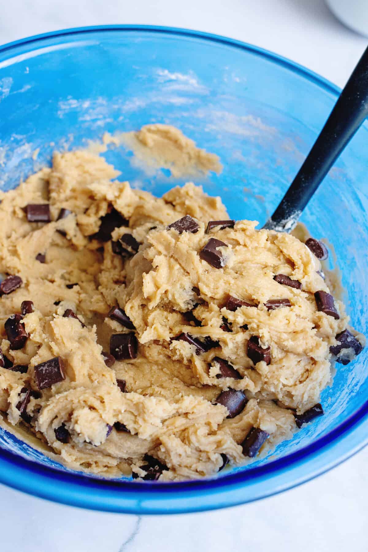 Chocolate chip cookie bar dough in a glass blue mixing bowl.