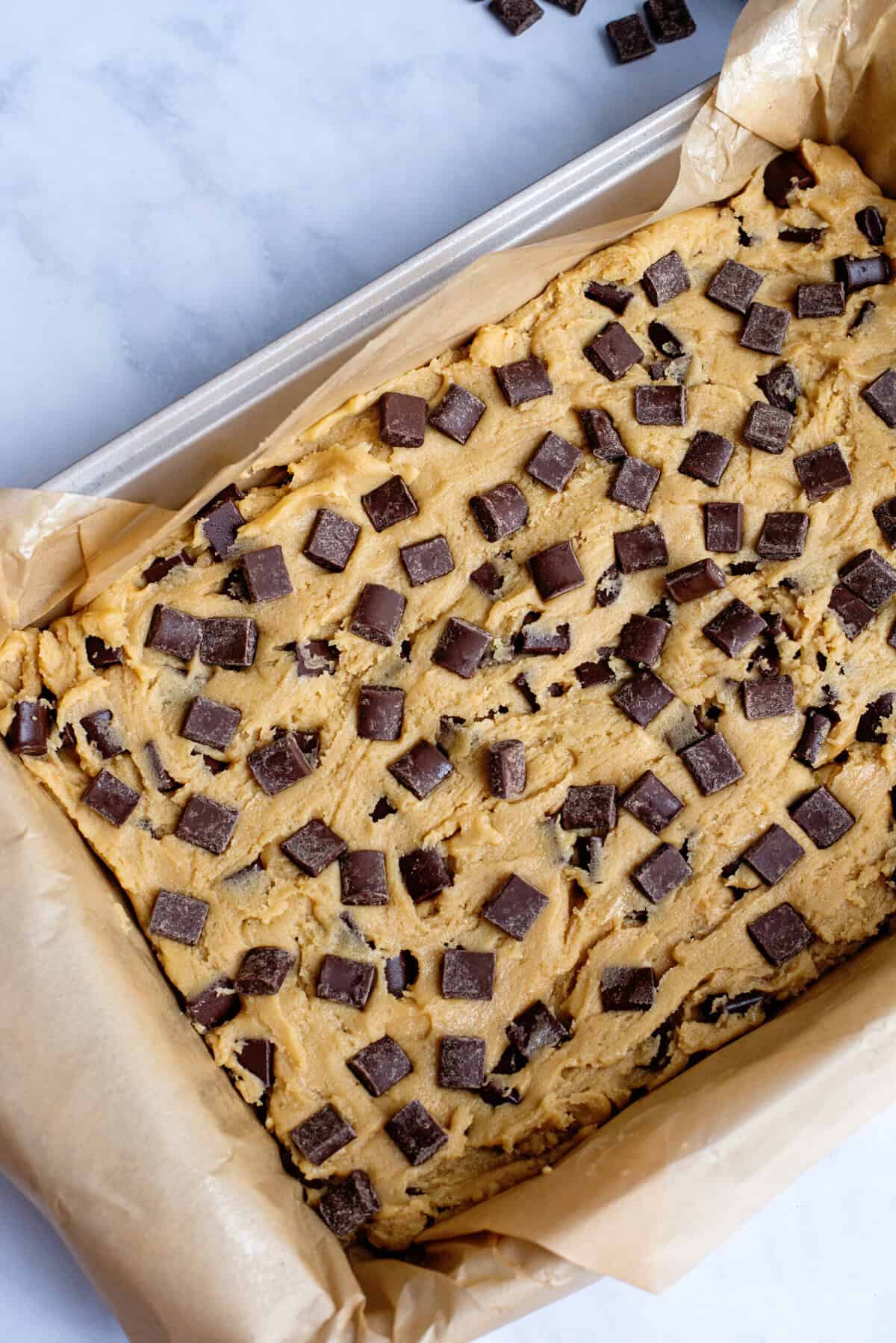 Chocolate chip cookie bar dough spread flat on a baking sheet with parchment paper.
