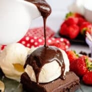 Hot fudge pouring from a pitcher onto a brownie topped with ice cream.