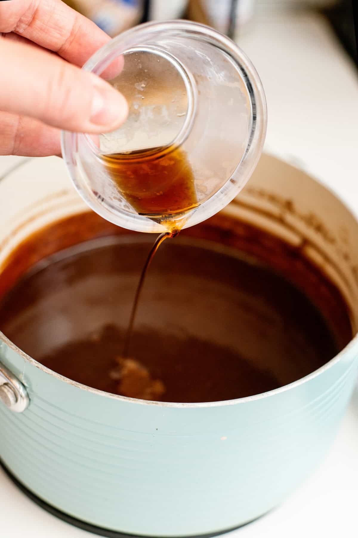 Pouring vanilla extract into a pot of hot fudge.