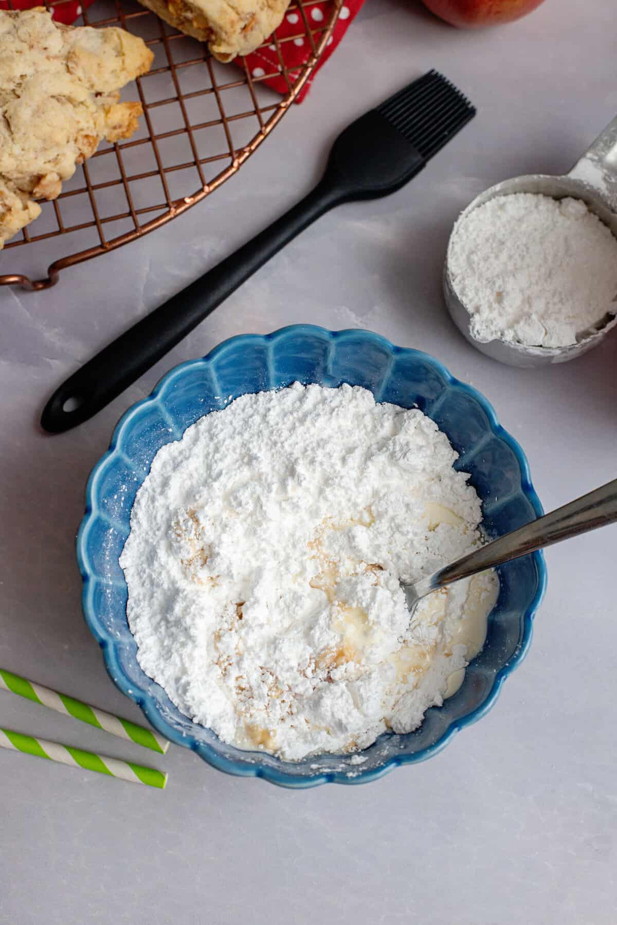 Powdered sugar, maple syrup, and milk in a blue bowl.