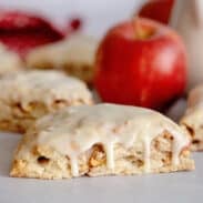 Glazed apple maple bakery scone with more scones and an apple in the background.