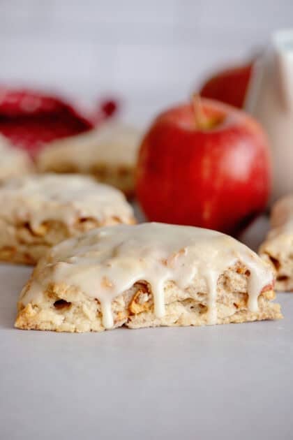 Glazed apple maple bakery scone with more scones and an apple in the background.