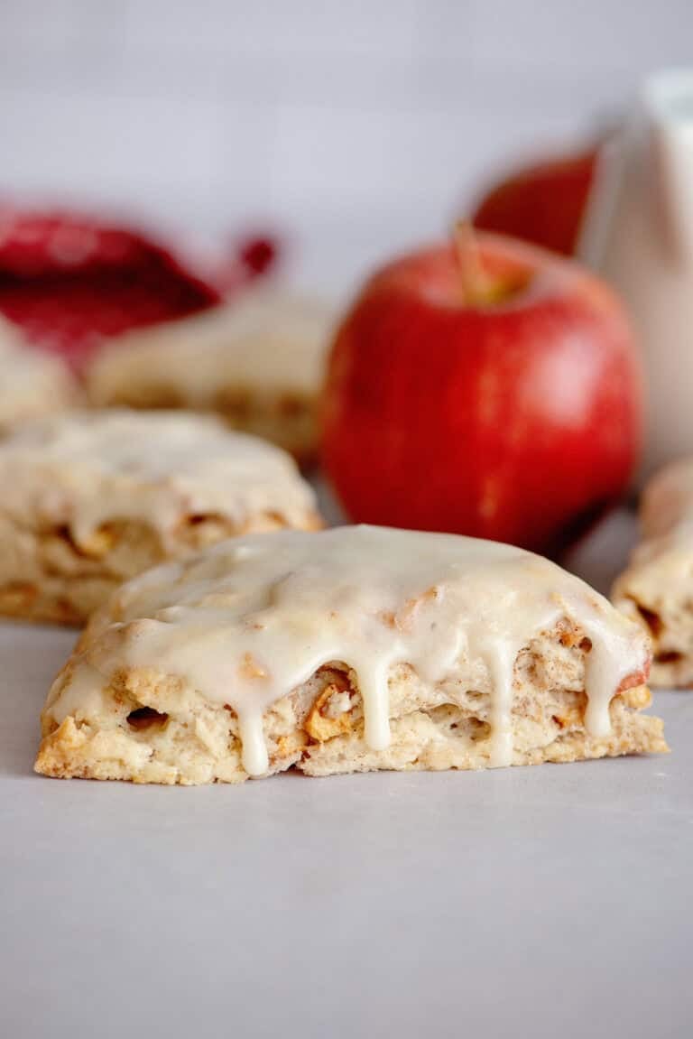 Glazed apple maple bakery scone with more scones and an apple in the background.