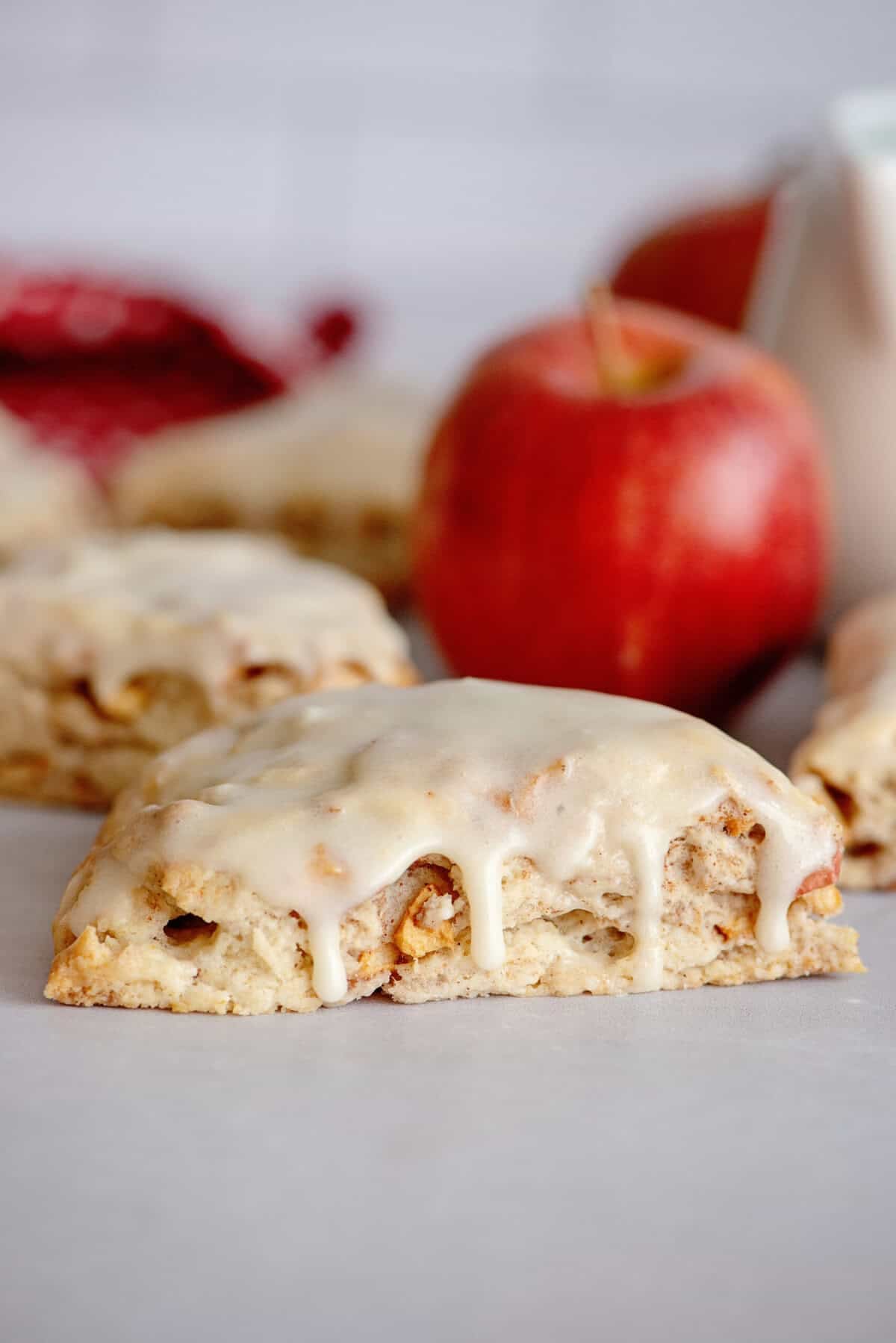 Glazed apple maple bakery scone with more scones and an apple in the background.