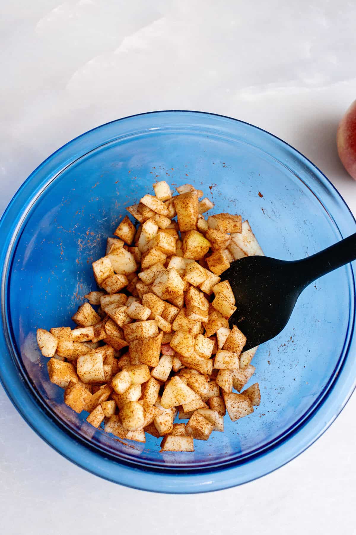 Tossing diced apples with cinnamon in a mixing bowl.