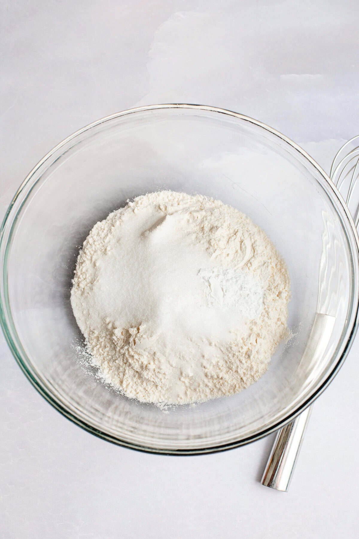 A glass mixing bowl of flour, sugar, baking powder, and salt.