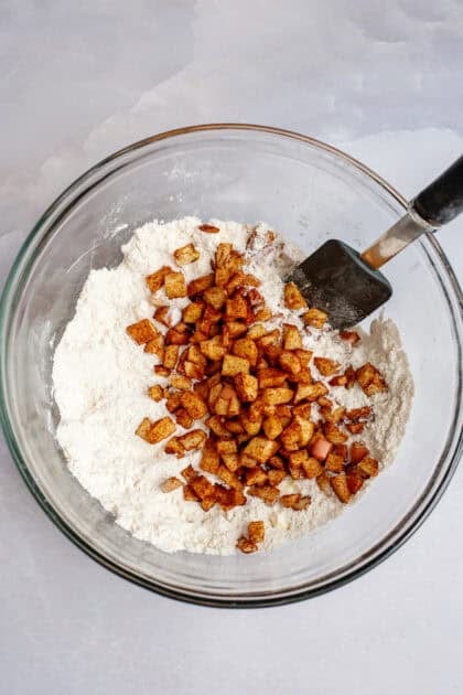 Folding diced cinnamon baked apples into a mixing bowl with butter and dry ingredients.