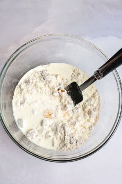 Mixing wet ingredients with the dry ingredients in a mixing bowl.