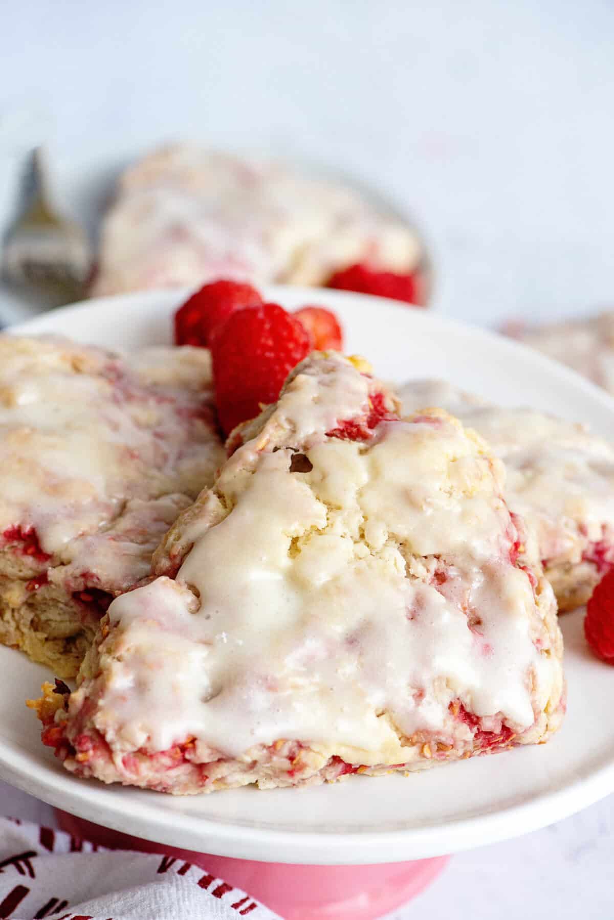Two glazed raspberry scones on a white plate.