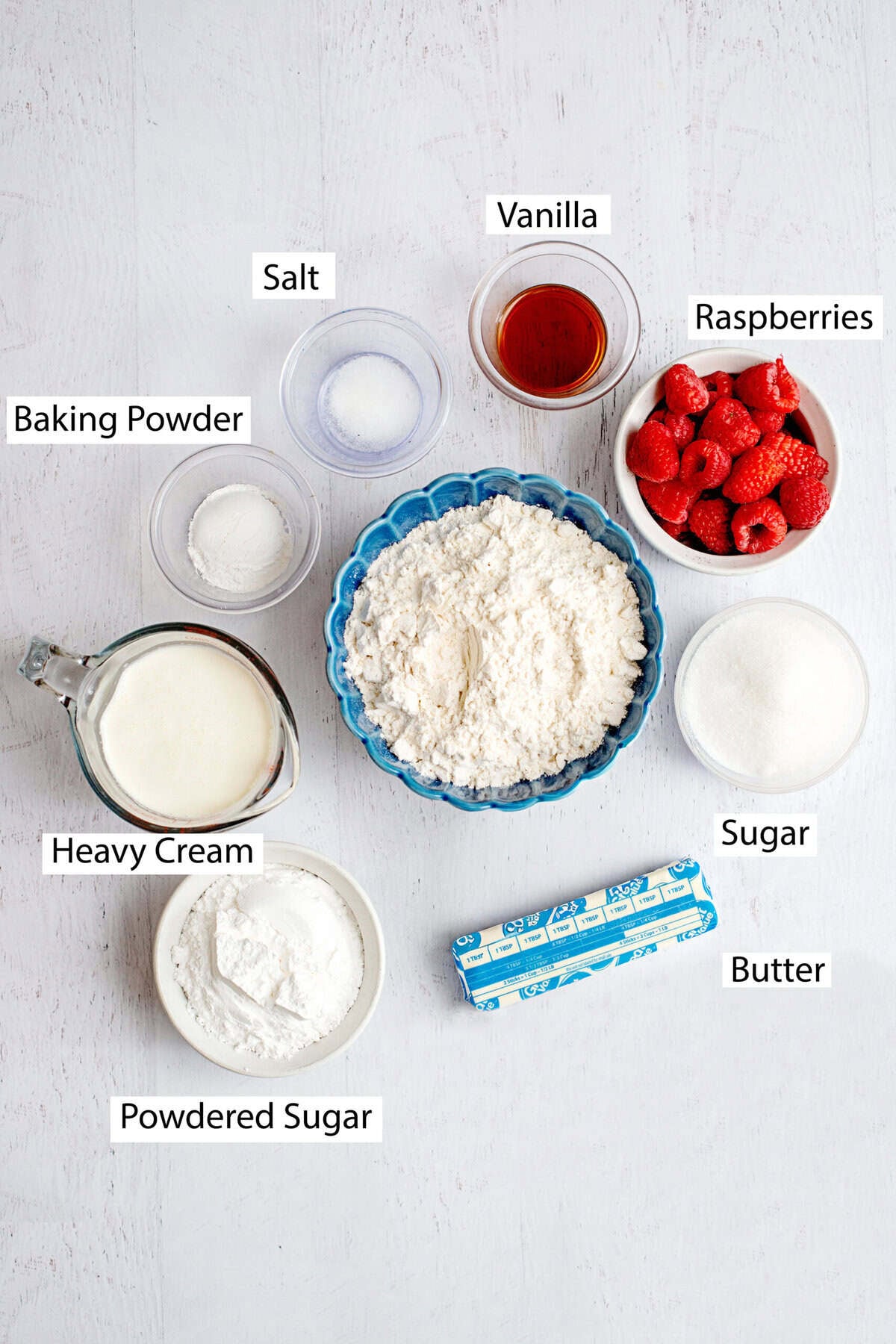 Ingredients for glazed raspberry scones include all-purpose flour, sugar, baking powder, salt, butter, raspberries, heavy cream, vanilla extract, powdered sugar, and milk.