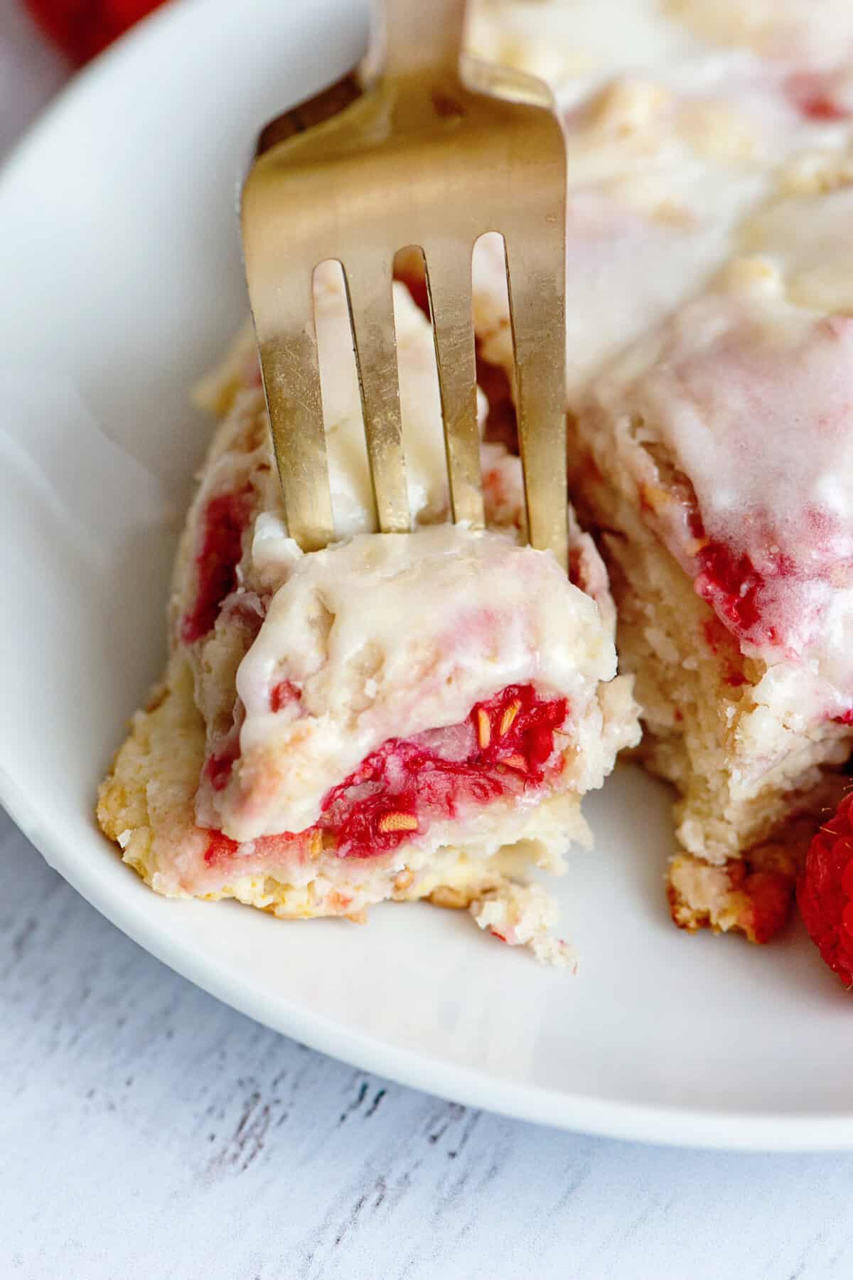 Close-up of fork digging into a piece of glazed raspberry scone.