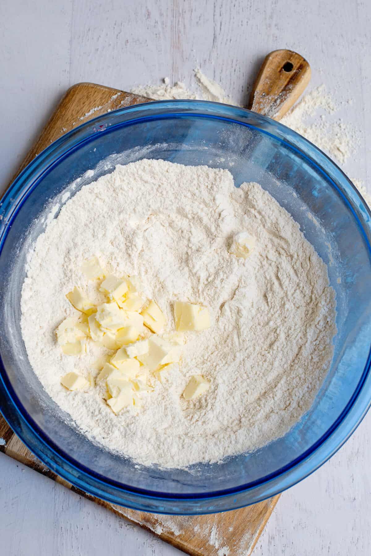 Cold, cubed butter in a blue mixing bowl of dry ingredients.