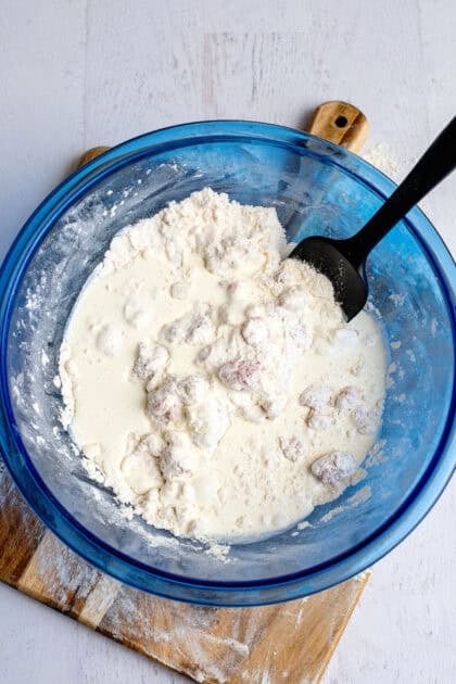 Mixing wet ingredients with dry ingredients in a glass blue mixing bowl.