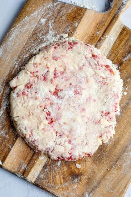 Raspberry scone dough formed into a thin circle on a cutting board.
