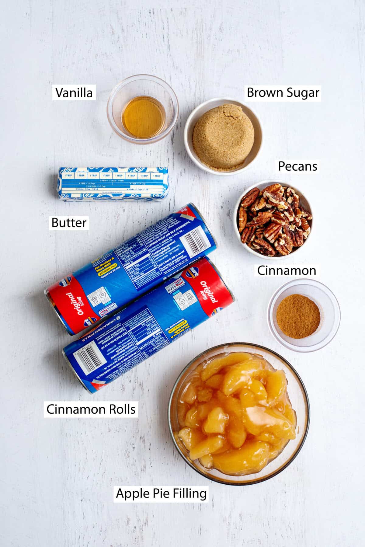 Ingredients for apple pie cinnamon roll monkey bread, including cinnamon rolls, apple pie filling, pecans, brown sugar, cinnamon, butter, and vanilla extract.