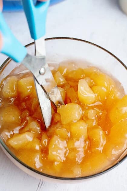 Cutting apple pie filling with scissors in a glass bowl.