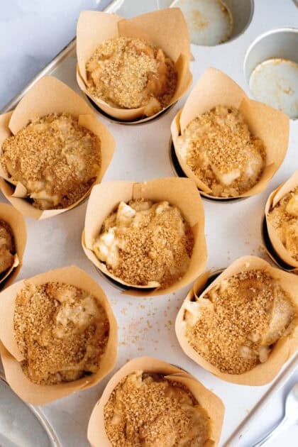 Cinnamon sugar sprinkled on muffin dough in a muffin pan.