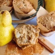 Brown butter pear muffins, with one sliced open next to a fresh pear.