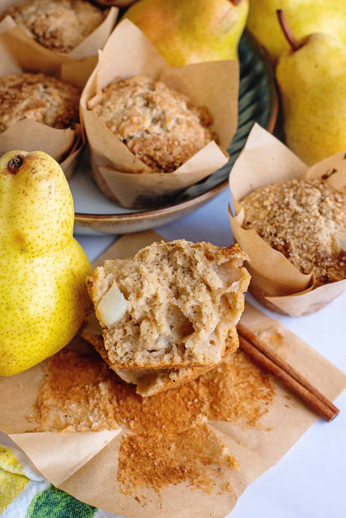 Brown butter pear muffins, with one sliced open next to a fresh pear.
