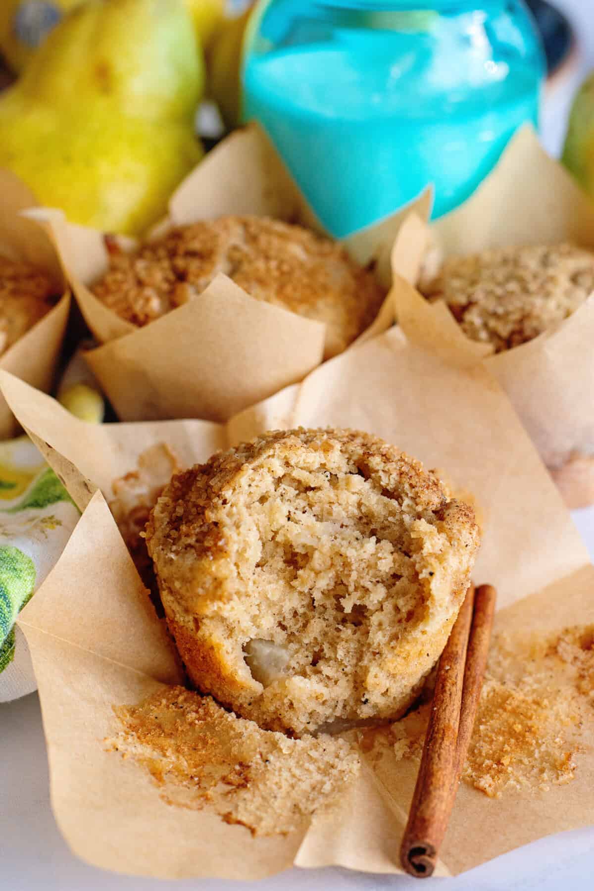 Brown butter pear muffin with a bite taken out of it with a cinnamon stick on the side.
