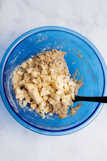 Folding chopped pears into dough in a glass blue mixing bowl.