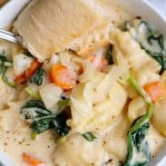 Creamy tortellini soup with crusty bread in a white bowl.