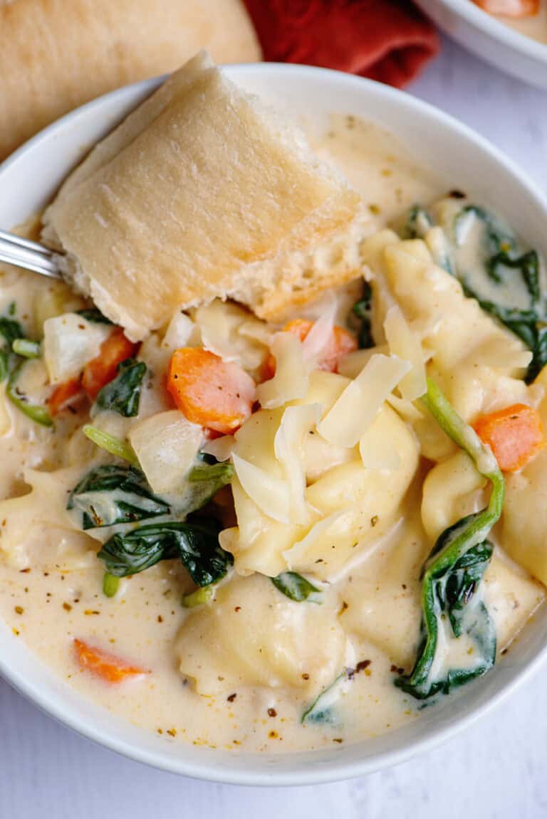 Creamy tortellini soup with crusty bread in a white bowl.