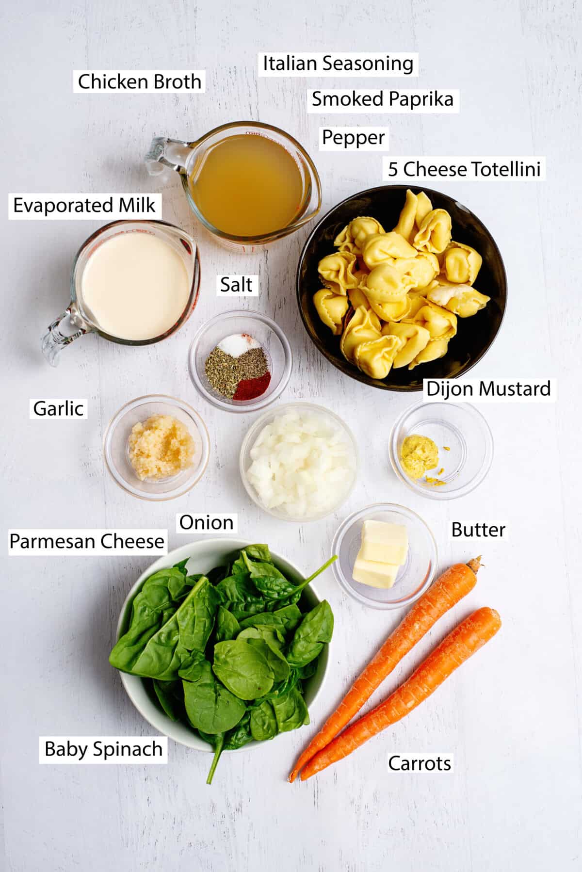 Ingredients for creamy tortellini soup, including butter, yellow onion, carrots, seasoning, chicken broth, Dijon mustard, tortellini, evaporated milk, baby spinach, and parmesan cheese.