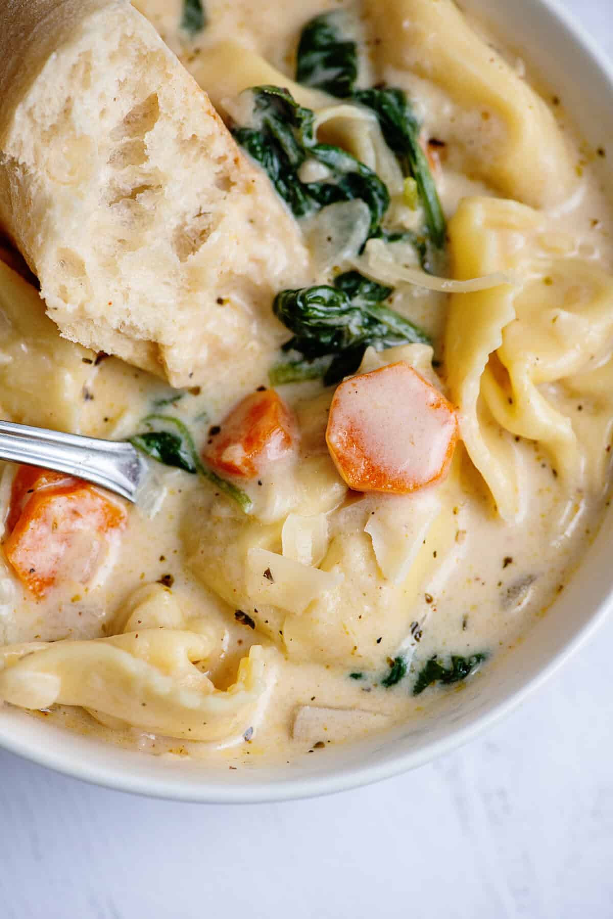 Creamy tortellini soup in a white bowl with a spoon.