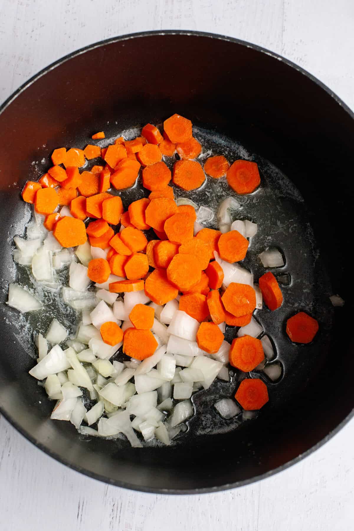 Onion and carrots sautéing in a pot.